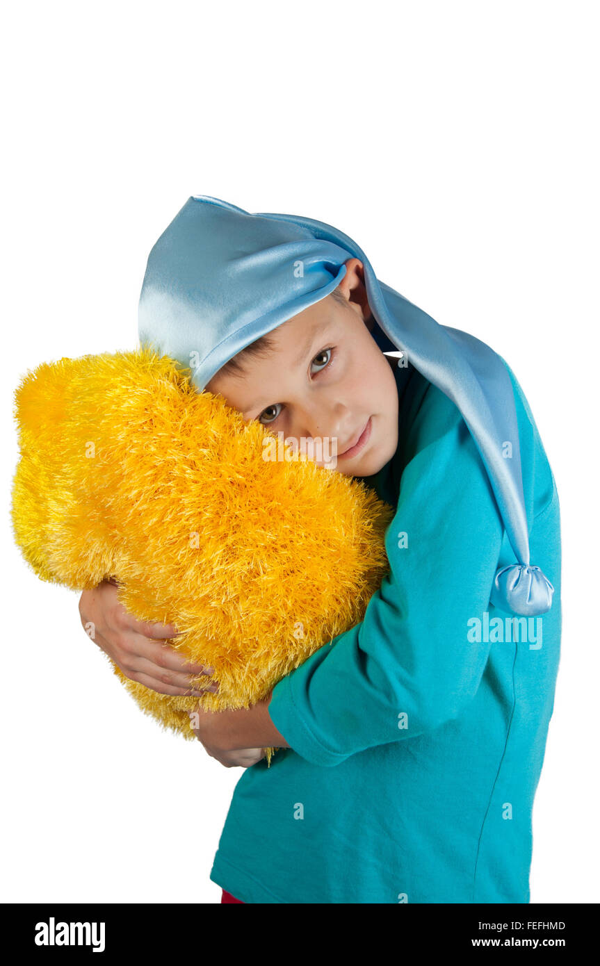 Boy in blue pajamas and sleeping hat holding yellow pillow isolated on