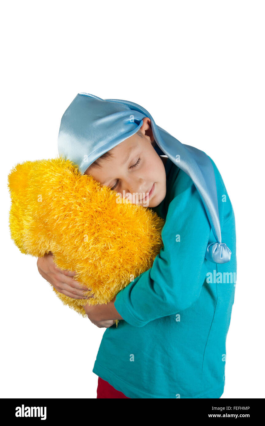 Boy in blue pajamas and sleeping hat holding yellow pillow isolated on