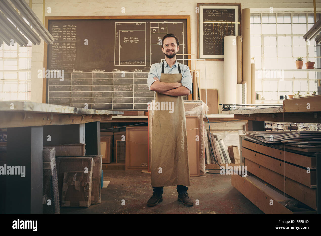 Full length portrait of a desigern craftsman confidently standing with his arms crossed in his workshop and smiling at the camer Stock Photo