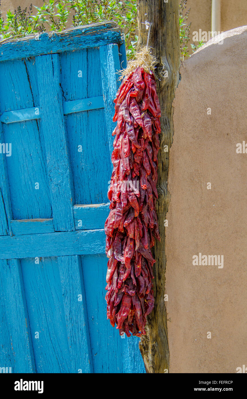 A "ristra" of dried red chiles hangs by and old gate in an adobe wall in Taos, New Mexico Stock Photo