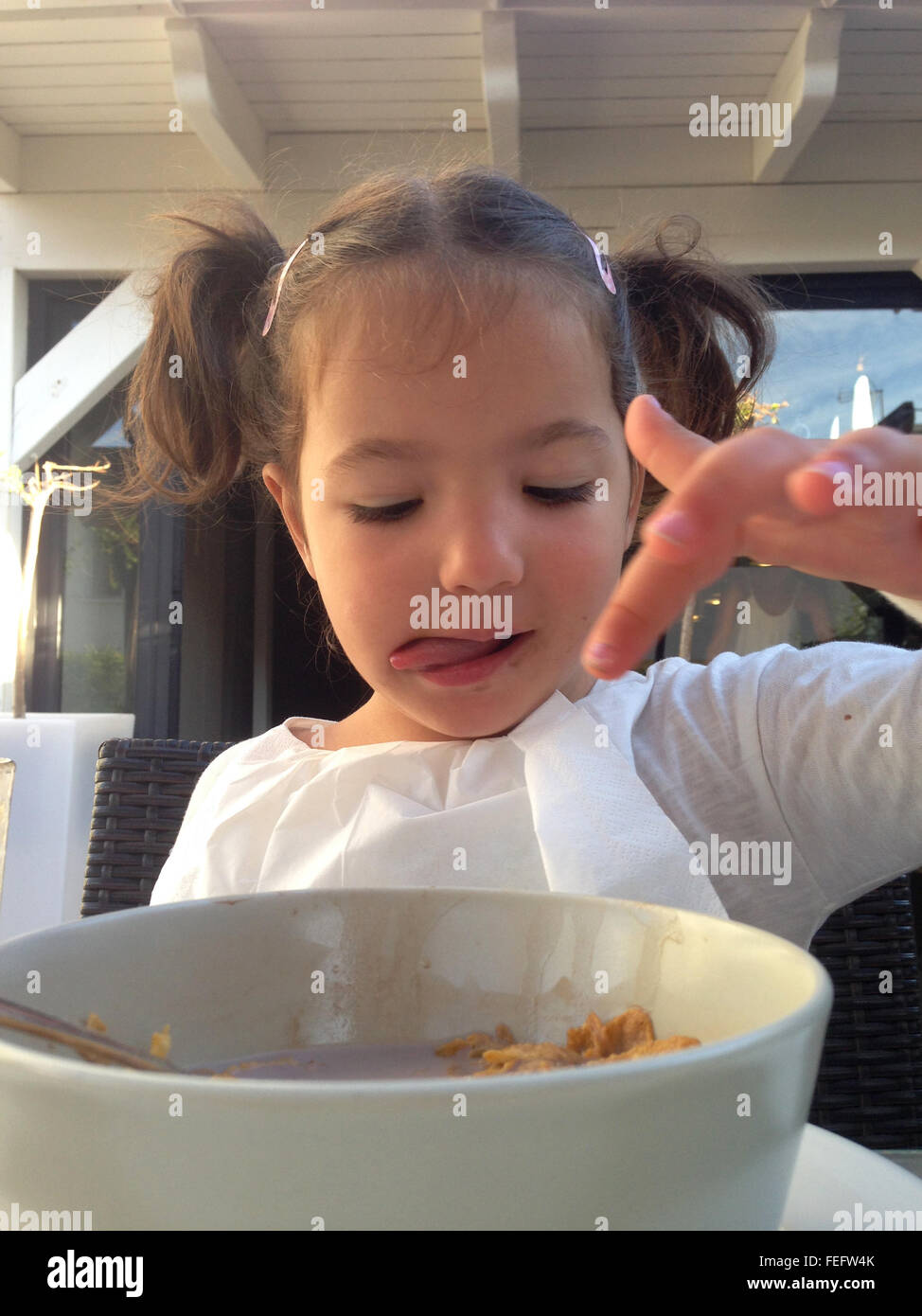 Child girl having a healthy breakfast outdoors. She is eating chocolate flakes and orange juice Stock Photo