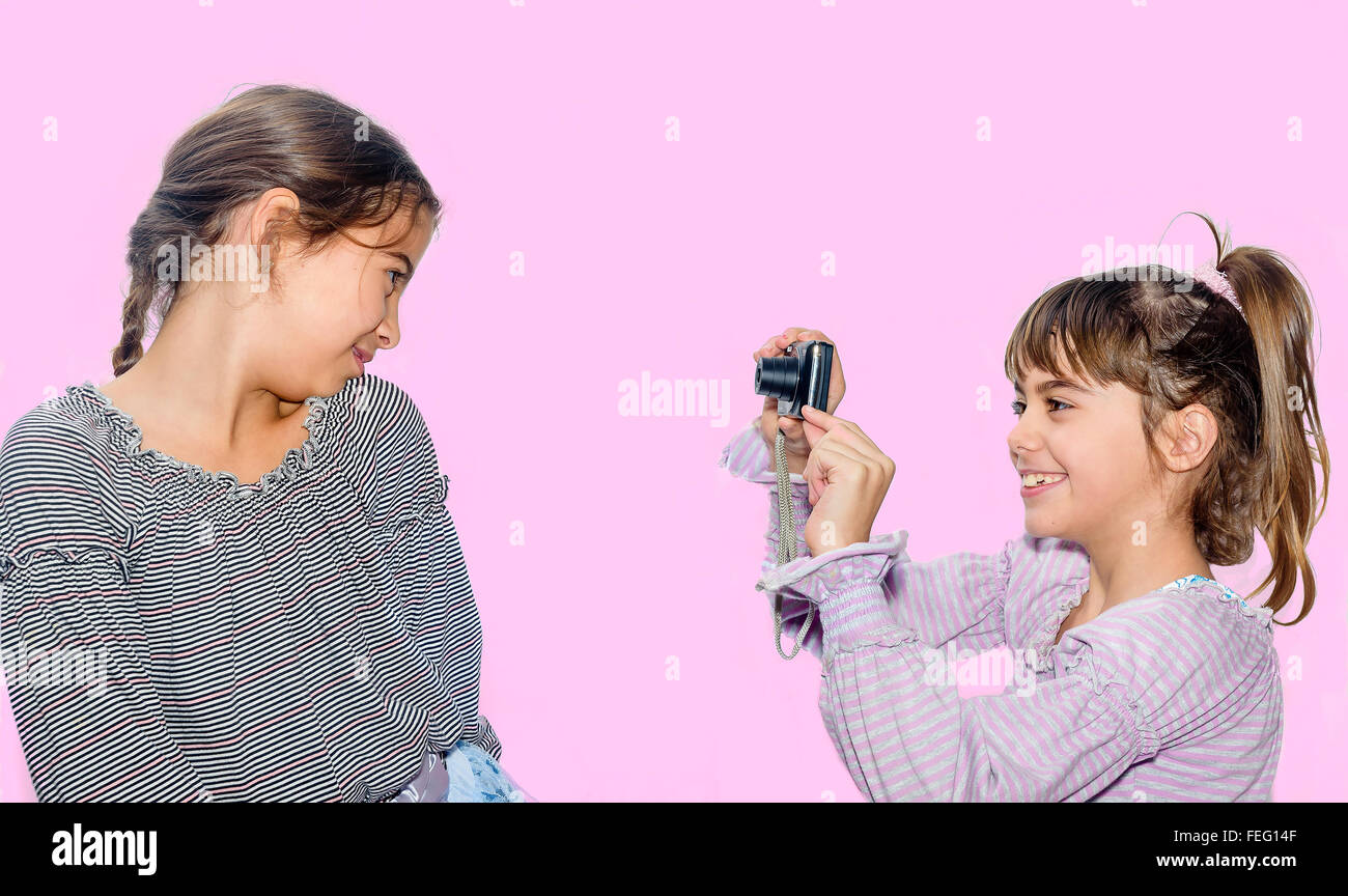 Little girl taking pictures of her sister with camera isolated on pink Stock Photo