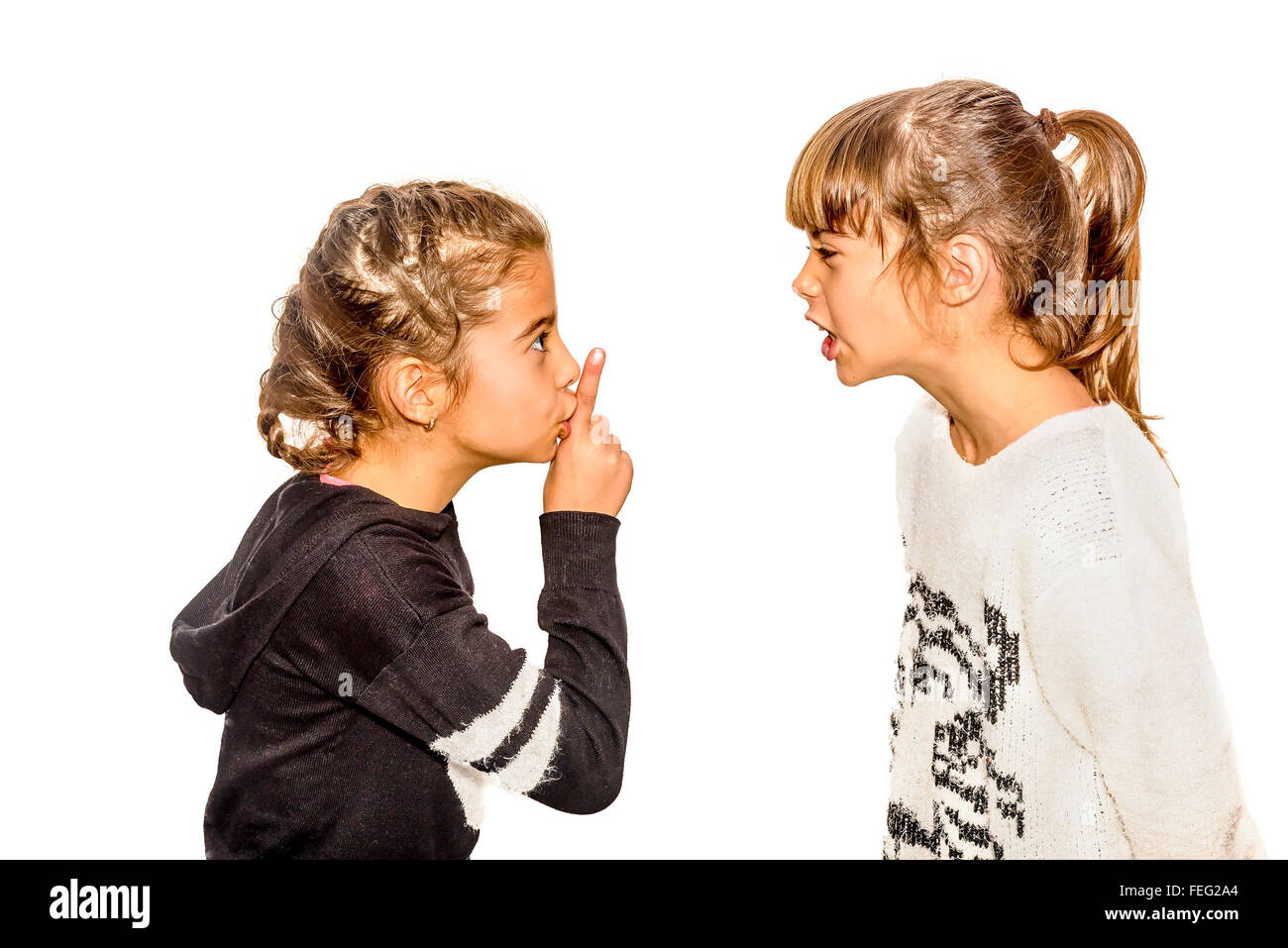 Little girl telling her sister to shut up with her finger on the mouth. A gesture of silence . Closeup-Isolated on white Stock Photo