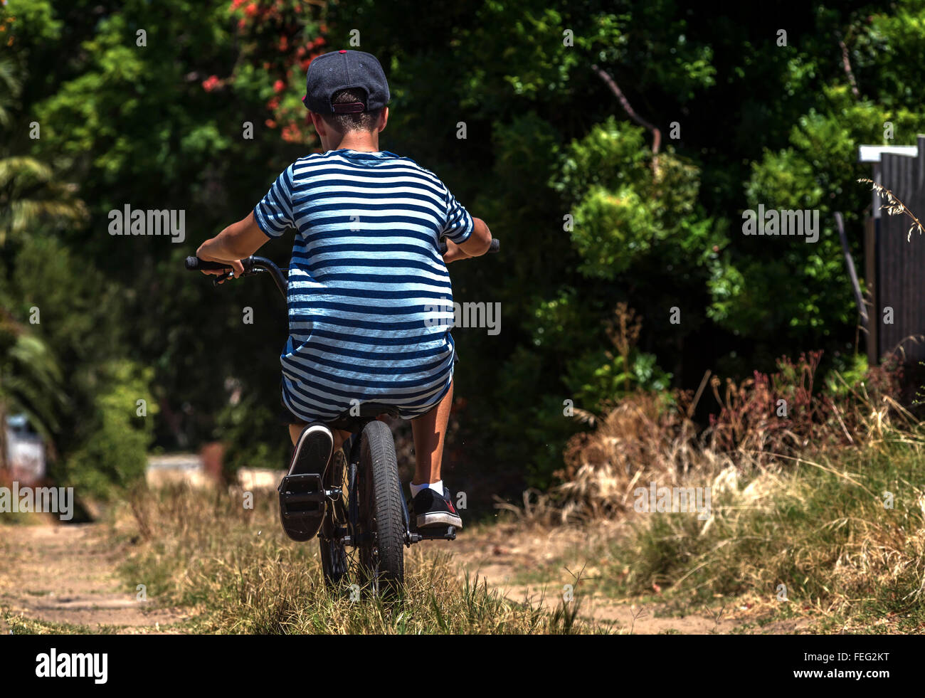 Boy with back to camera rides BMX bicycle down a scruffy back lane Stock Photo