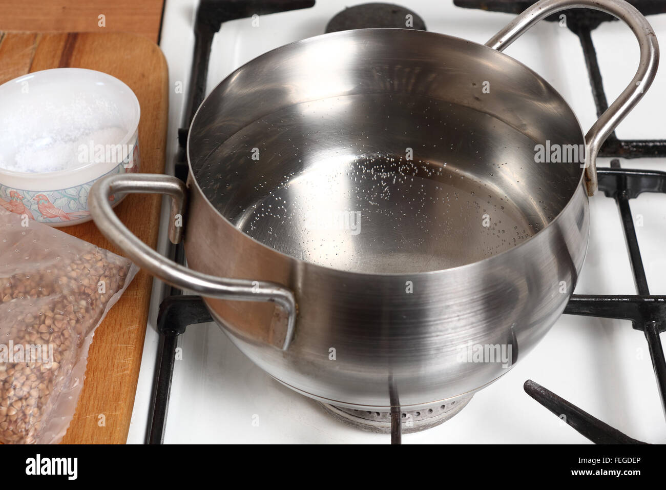 Boiling water into saucepan. Cooking buckwheat groats on gas stove