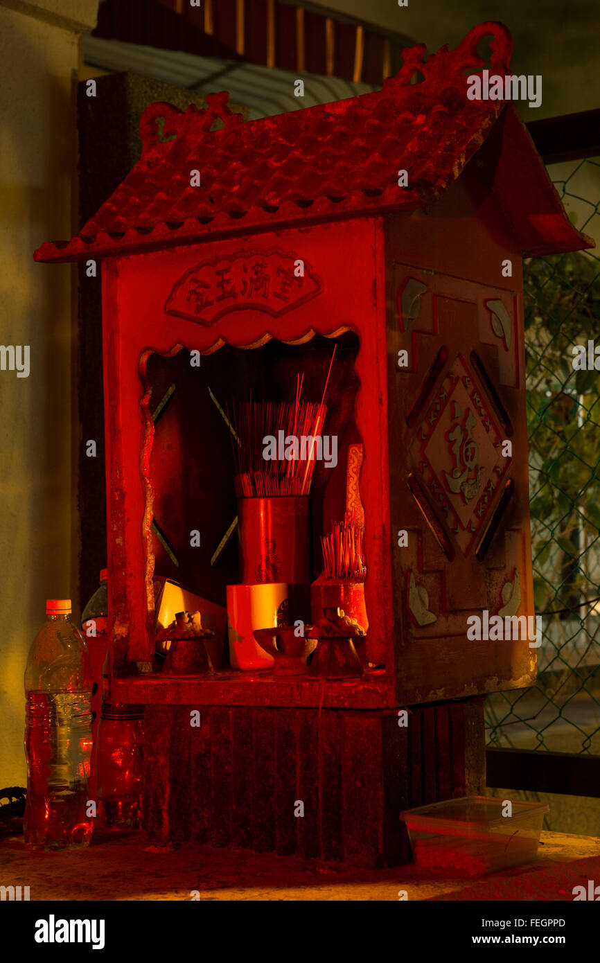 Mini Chinese temple. Night shot of an outdoor temple with candles incense and offering of fruit. Stock Photo