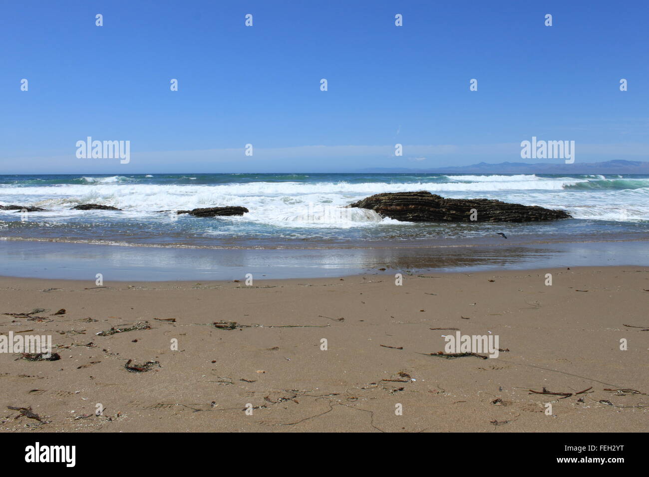 Waves crashing on and through the rocks on to the sandy beach , three ...
