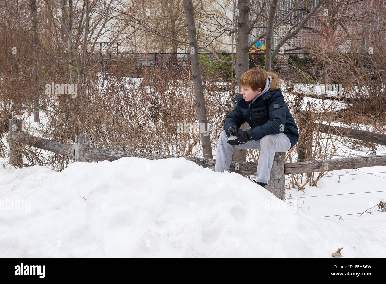 Young boy sitting on a wooden fence holding a snowball Stock Photo