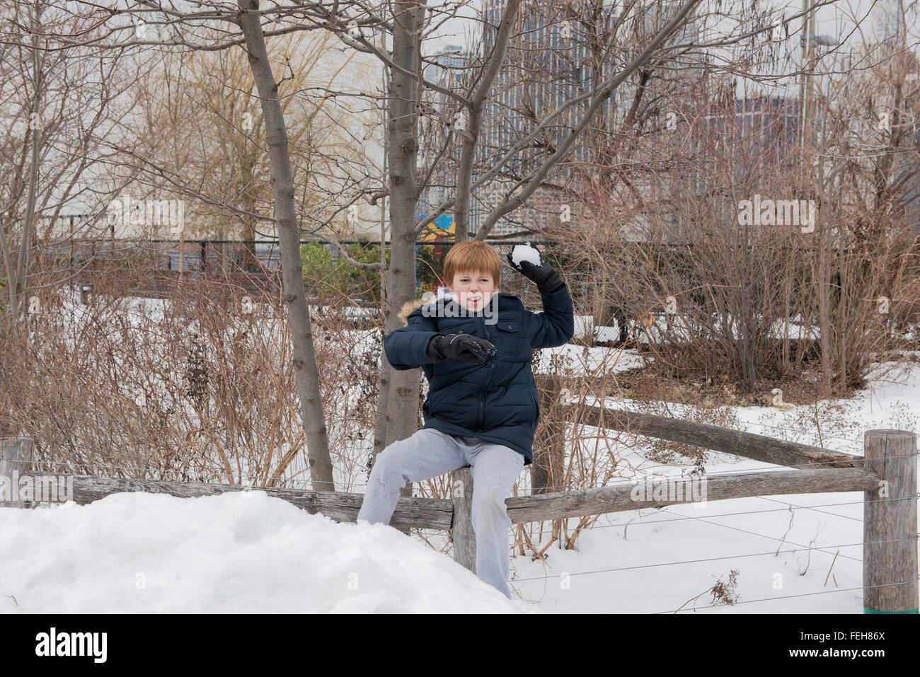 Young boy sitting on a wooden fence preparing to throw a snowball Stock Photo