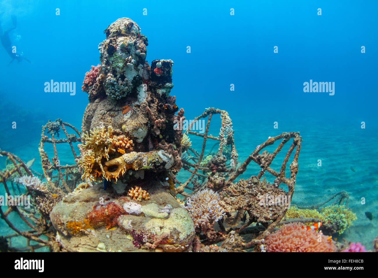 Buddha statue on the sea sand bottom on background of snorkeler swimming deep down into water to observe beautiful tropical reef Stock Photo