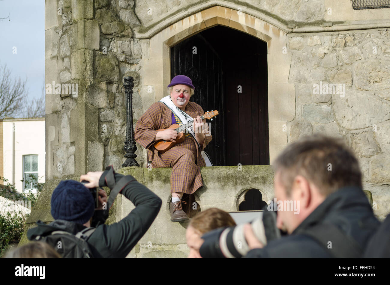 Hackney, London, UK. 7th February, 2016. A clown playing a ukelele poses for photographers outside All Saints Church in Haggerston ahead of the annual Clown Service in memory of Joseph Grimaldi - known as the King of Clowns. Credit:  Amanda Lewis/Alamy Live News Stock Photo