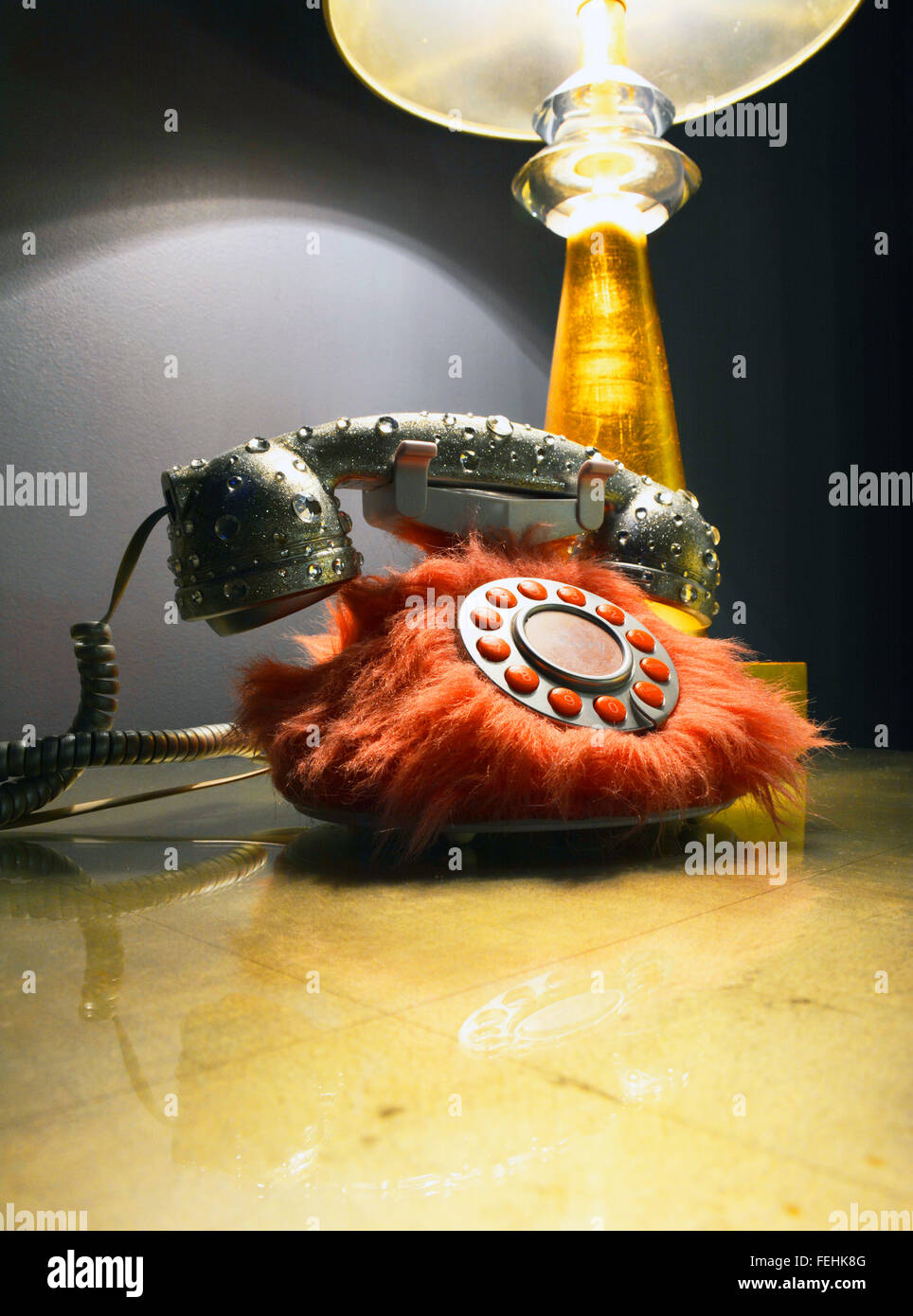 An unusual, artistic and wacky rotary phone decorated with orange fur and acrylic like bubbles on handset on table with lamp odd Stock Photo