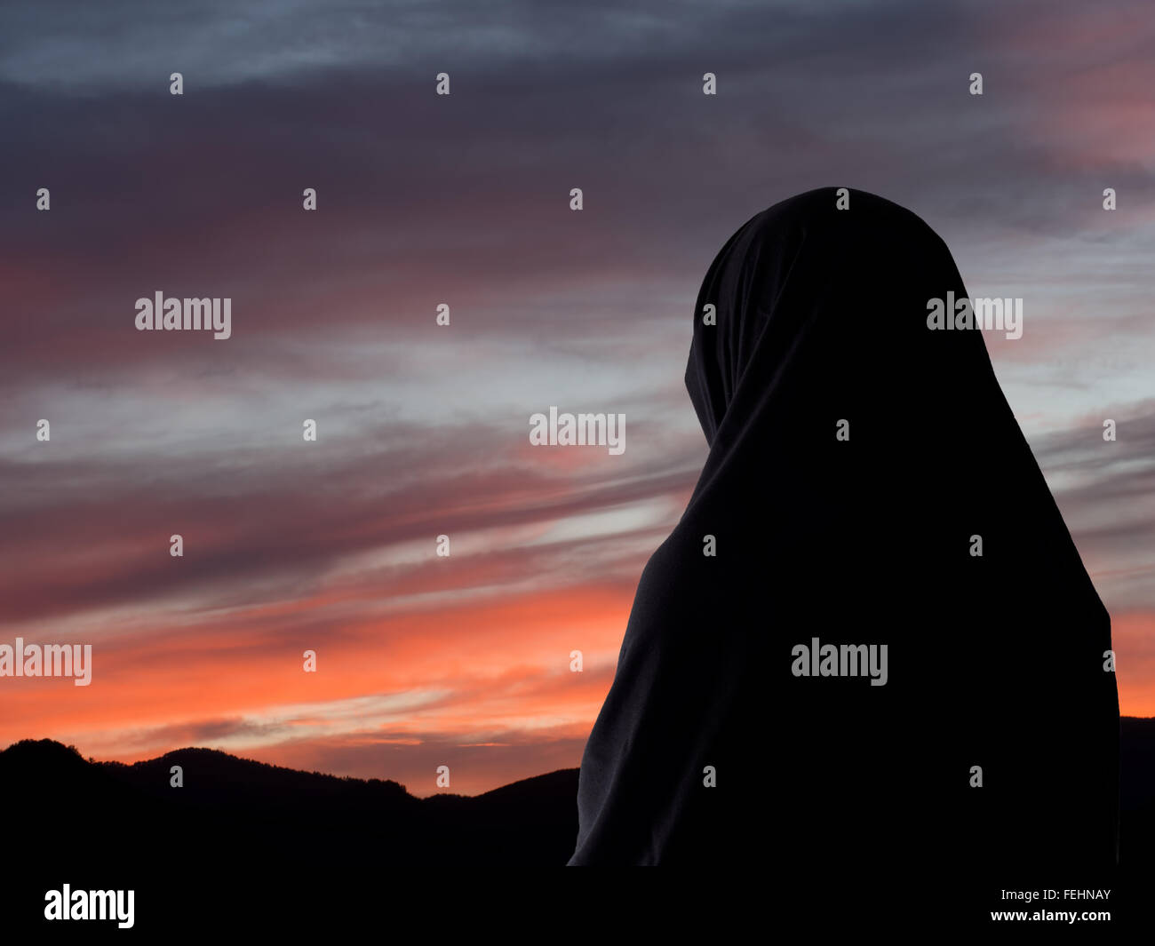 Evening prayers, Muslim woman in chador aganst sunset sky. Stock Photo