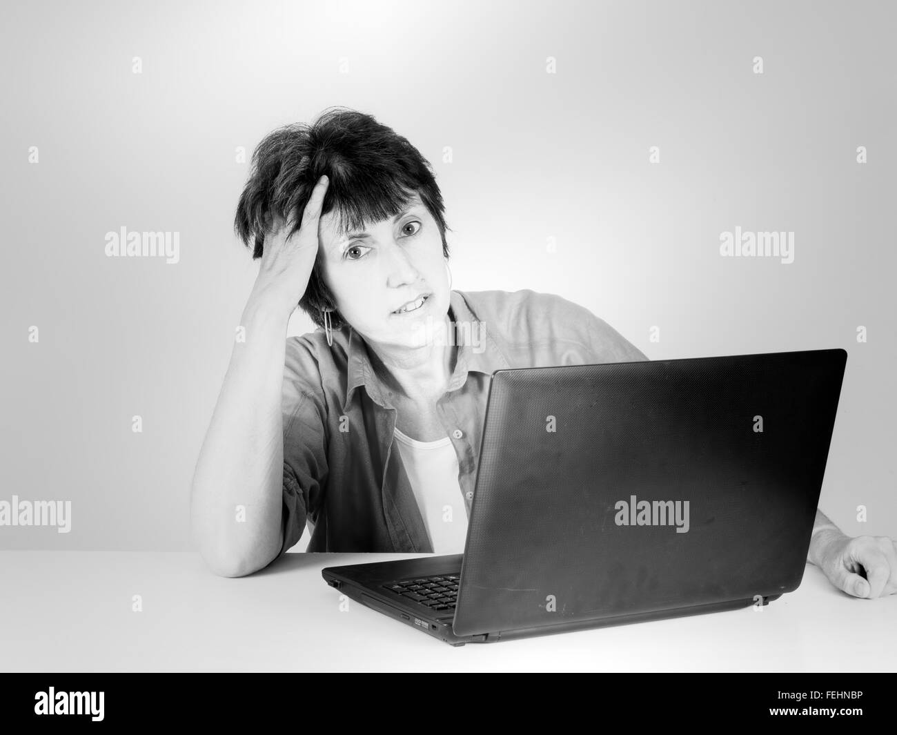 Middle aged woman with laptop, tired. Retro filtered monochrome image. Stock Photo