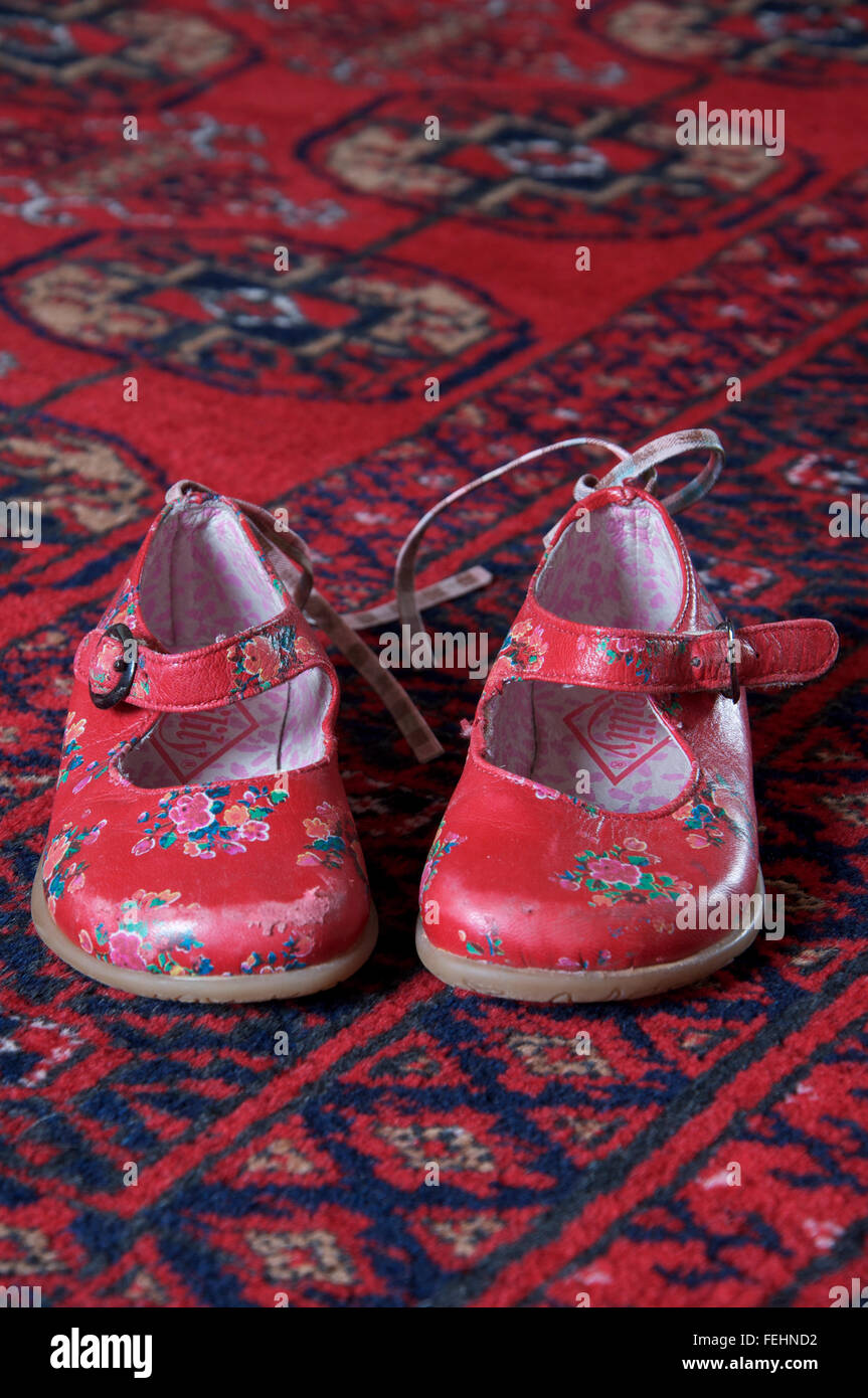 A well worn pair of little girl’s bright red shoes placed on a rug