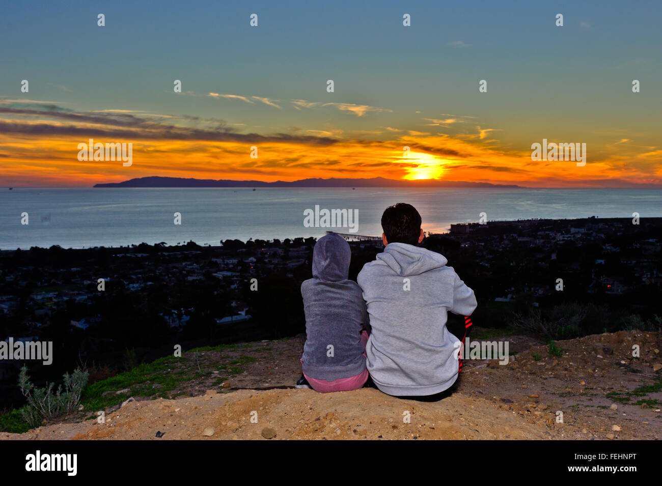 Man and child sitting together watching the sun drop below the horizon. Stock Photo