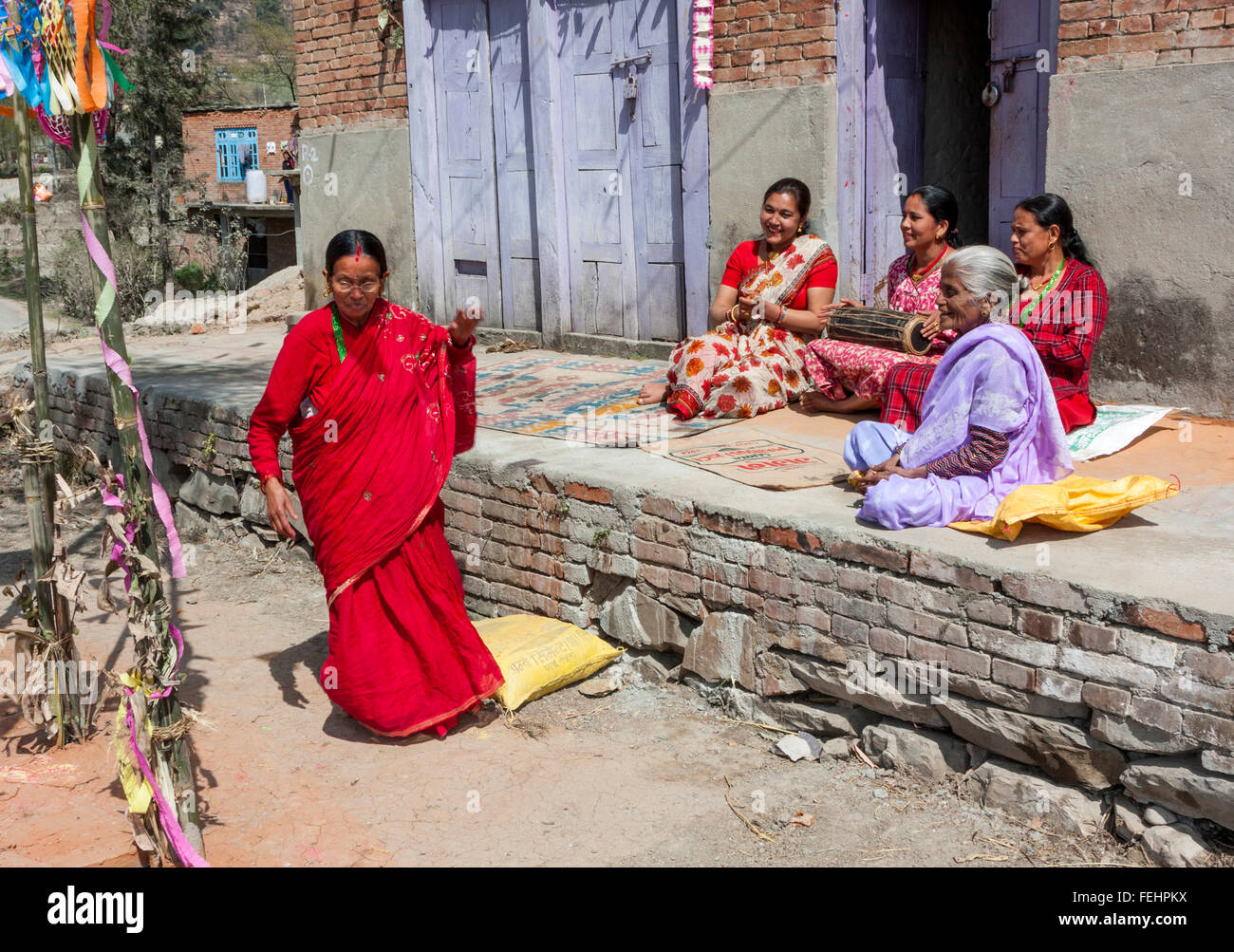 Bhaktapur, Nepal.  Middle-aged Woman Dances while Friends Play Drum and Clap while Sitting on Front Porch of their House. Stock Photo