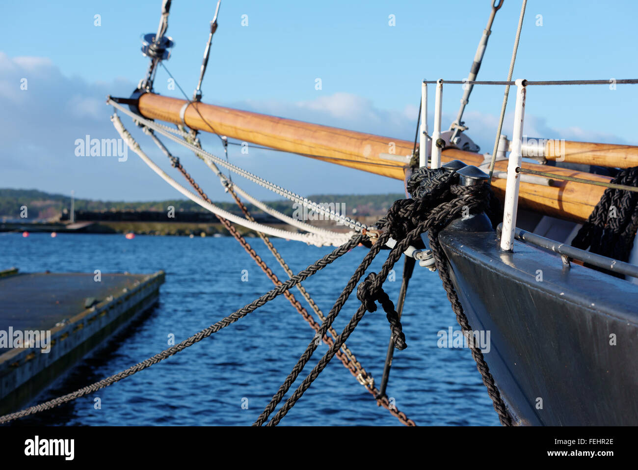 Lots of black ropes hold the black sailing ship. A wooden bowsprit