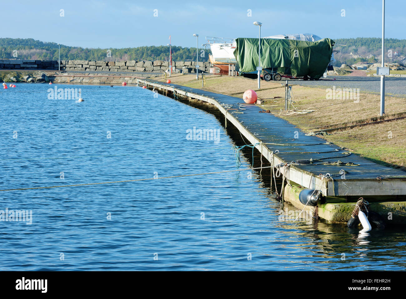 An empty wooden pier and three boats up on land in the distance. A rope is stretched in the foreground out over the water. Stock Photo