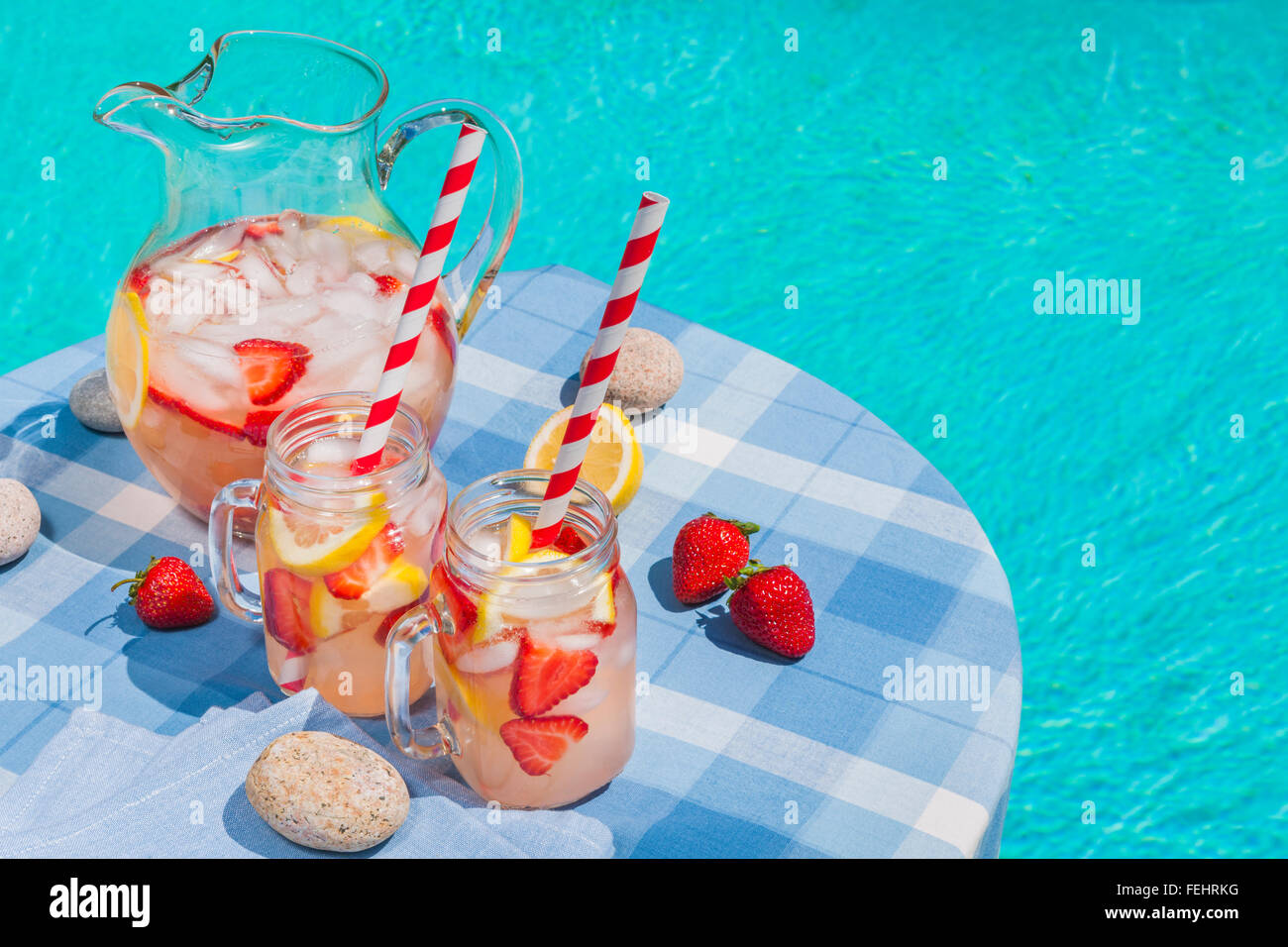 Ice cold homemade strawberry lemonade in jug and glasses with paper straws on outdoor pool side table in summer with copy space Stock Photo