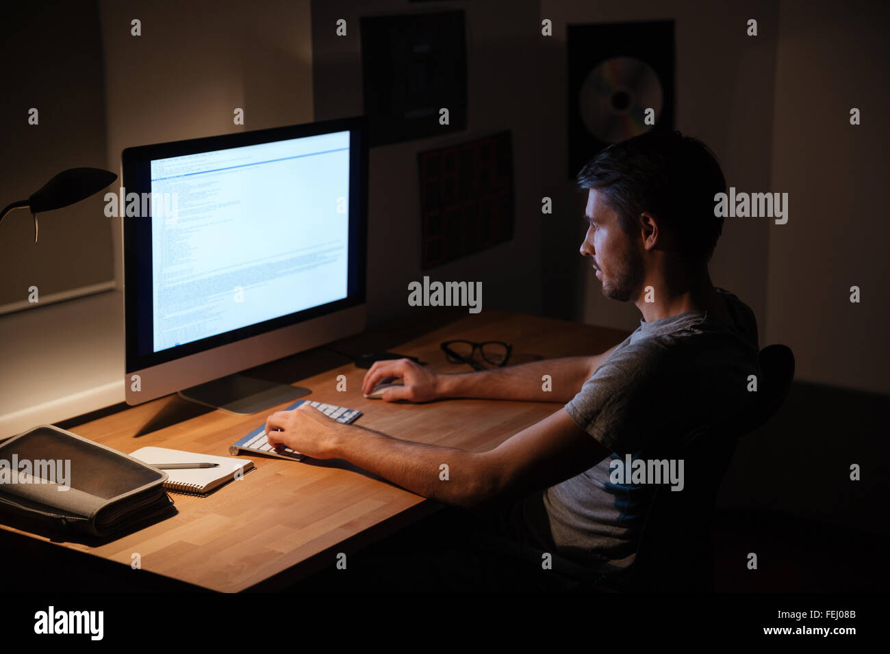Handsome young man sitting in dark room and using computer Stock Photo
