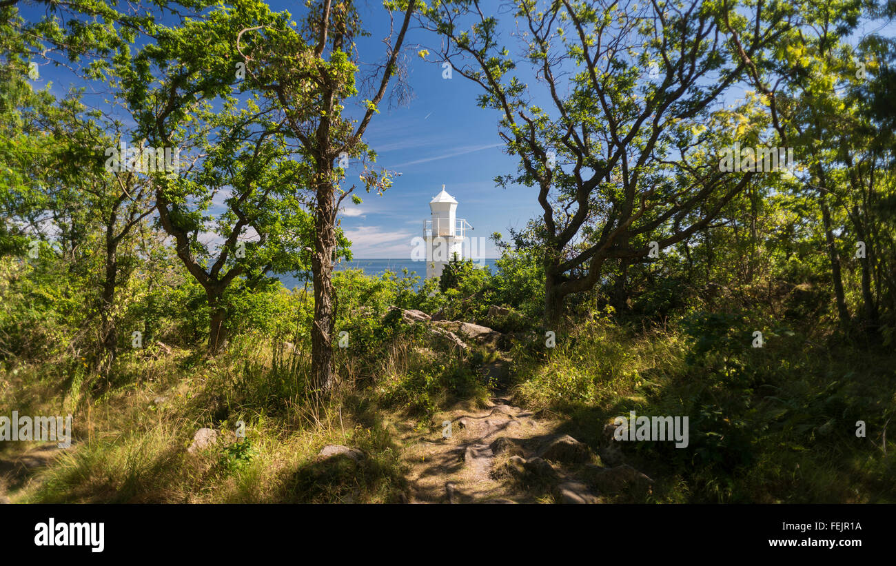 White lighthouse in the bright sunlight behind trees in the Stenshuvud National Park on the Baltic Coast of Skane, south Sweden Stock Photo