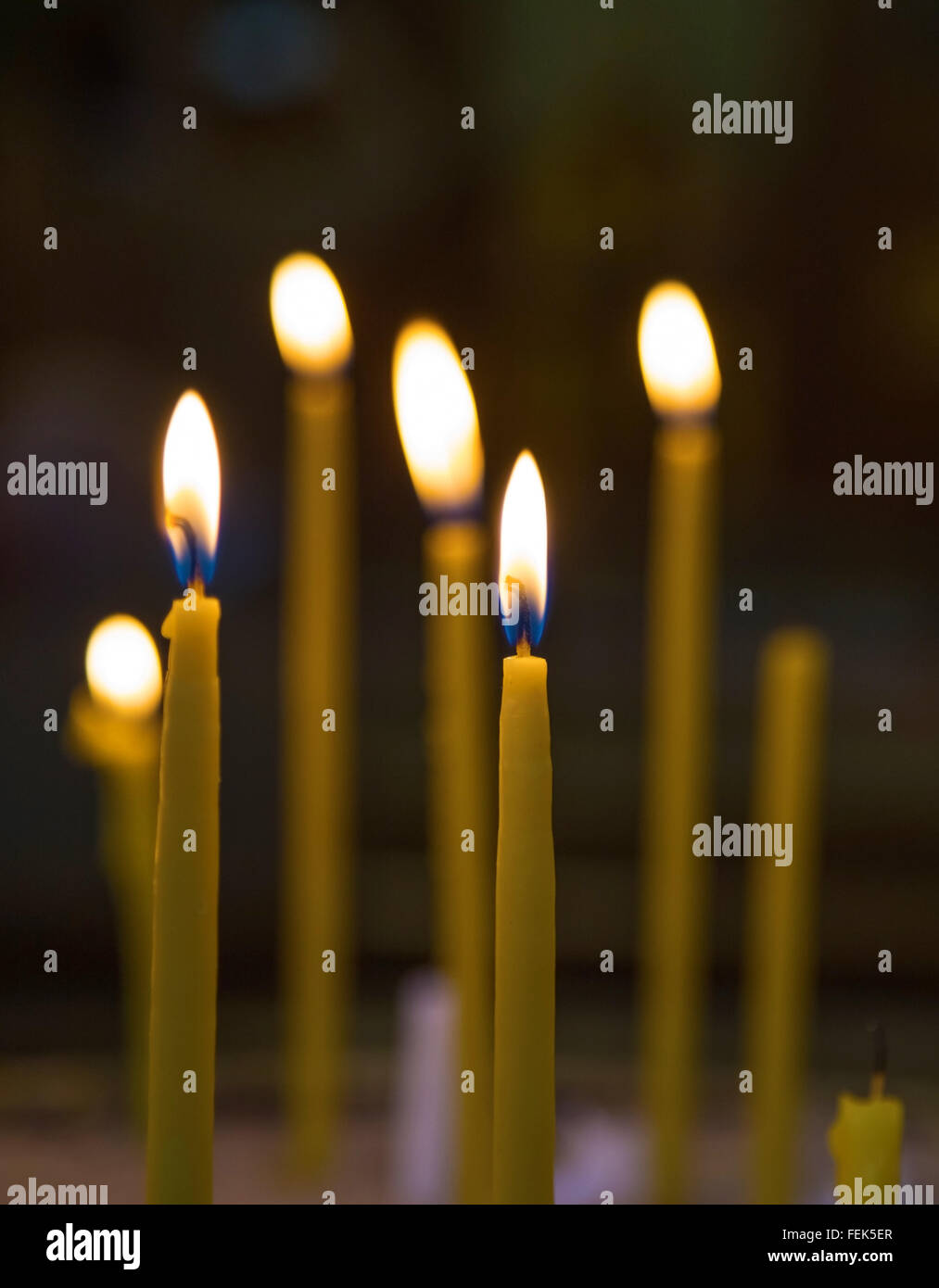 Lighted wax candles in a church burning in the twilight Stock Photo