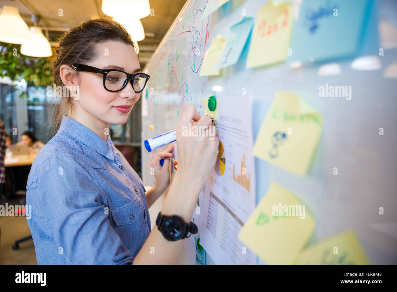 Young woman writing business plan on whiteboard in office Stock Photo