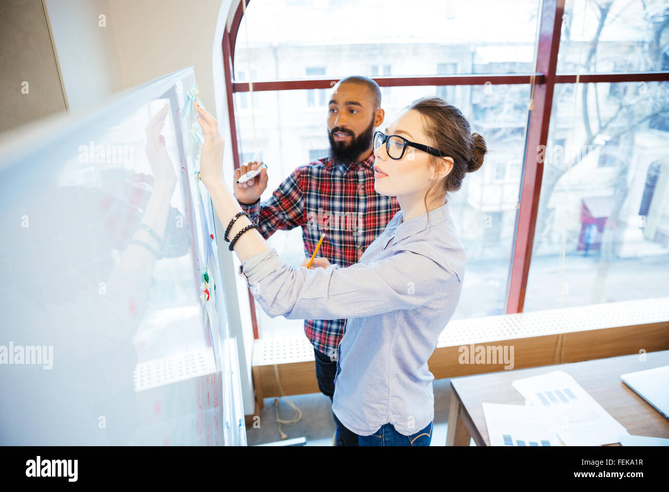 Concentrated man and woman students standing and writing on whiteboard in classroom Stock Photo