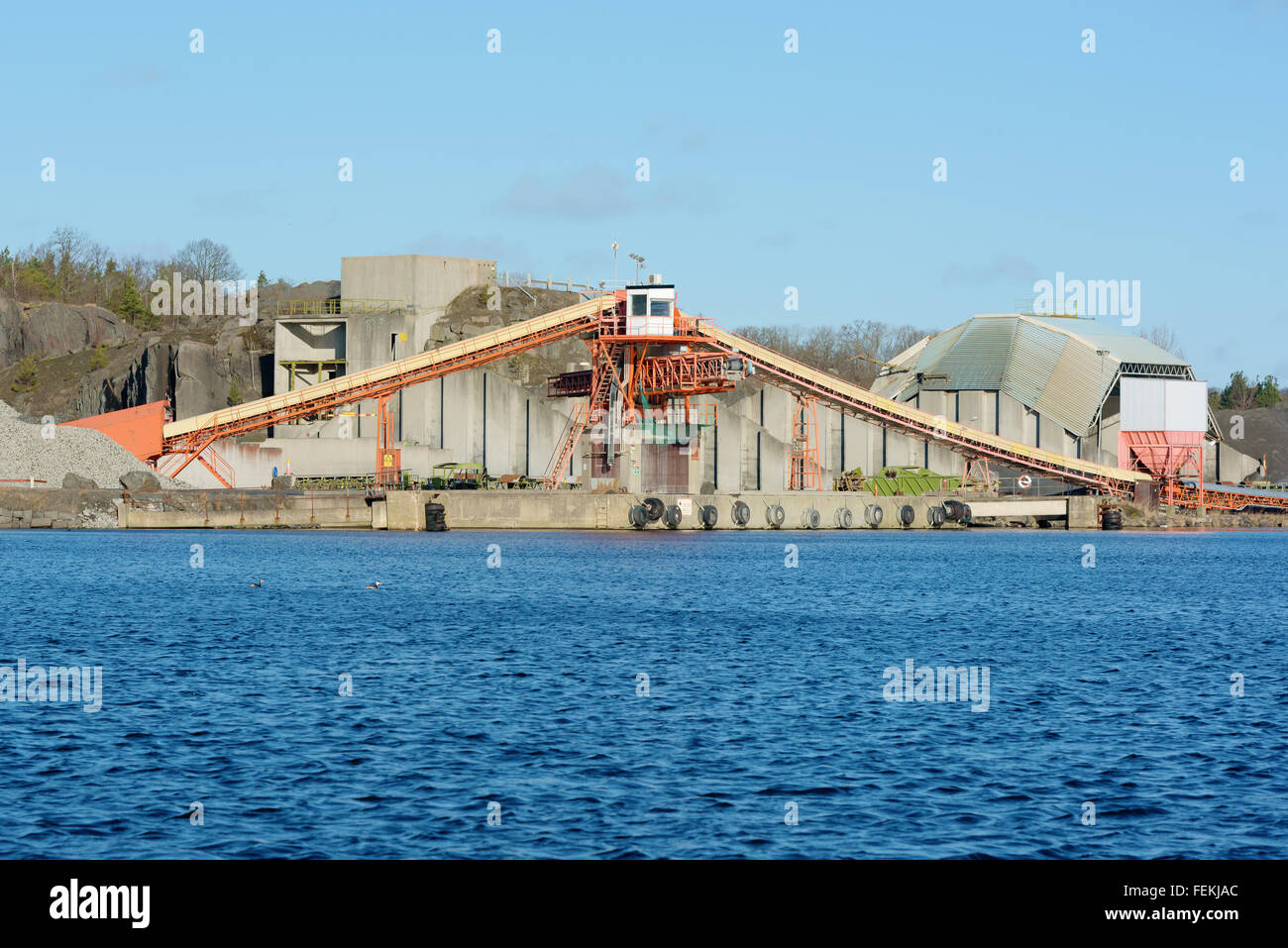 A loading facility in a quarry close to water. Gravel and stone is transported on curved conveyor belts up to the tower that dep Stock Photo