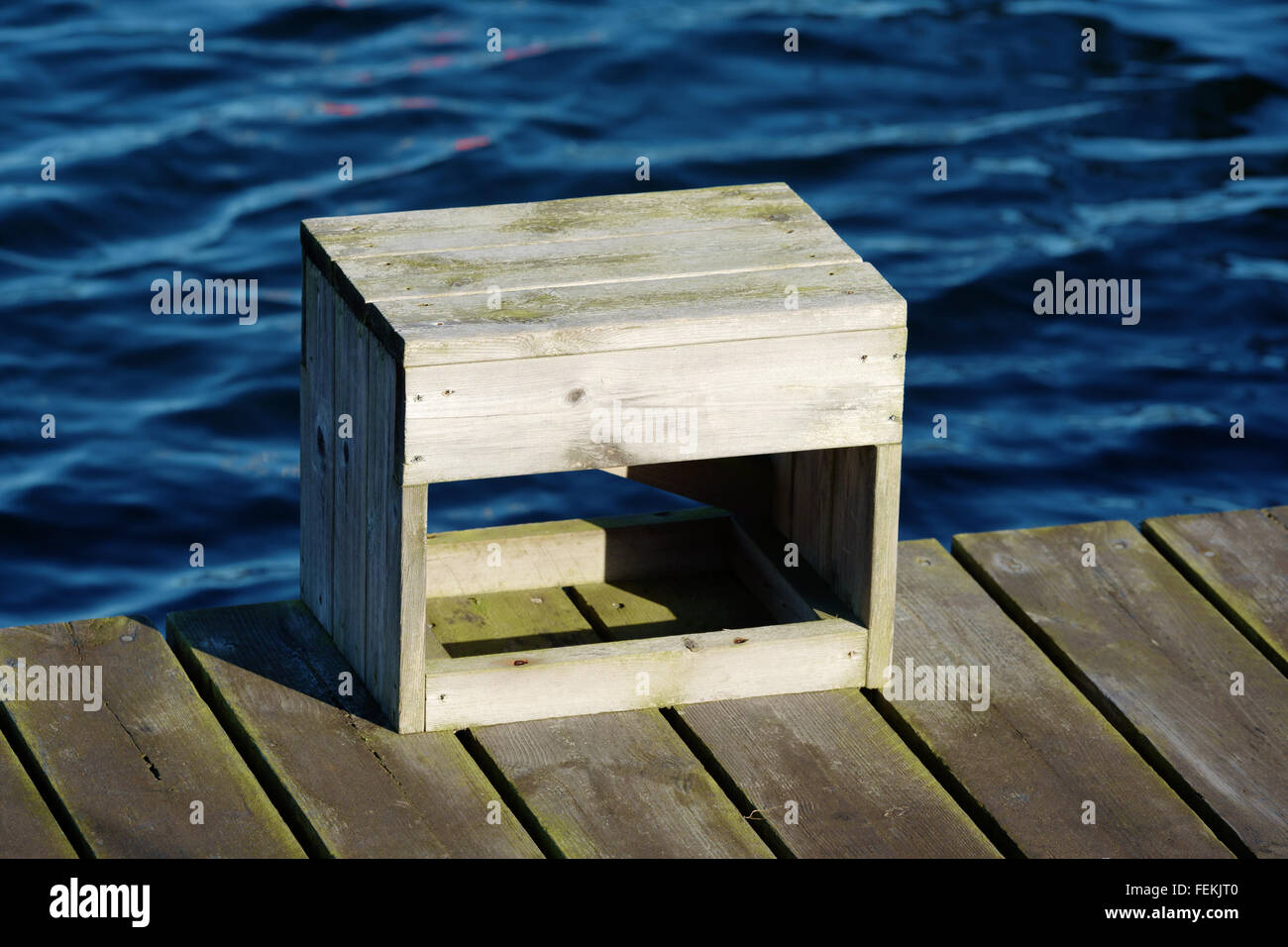 A wooden crate stand alone close to the edge of a pier with water in background. Stock Photo