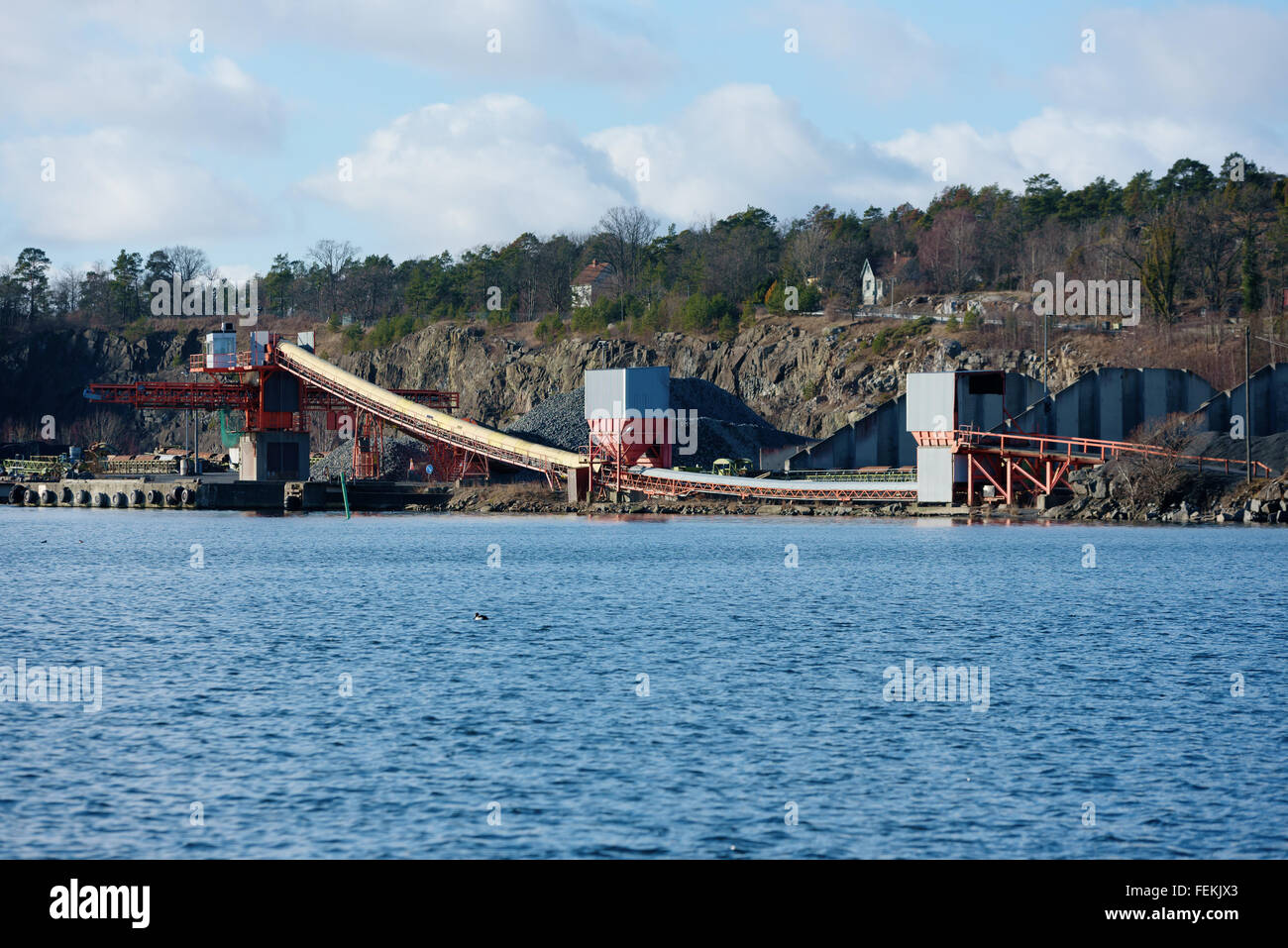 A loading facility in a quarry close to water. Gravel and stone is transported on curved conveyor belts up to the tower that dep Stock Photo