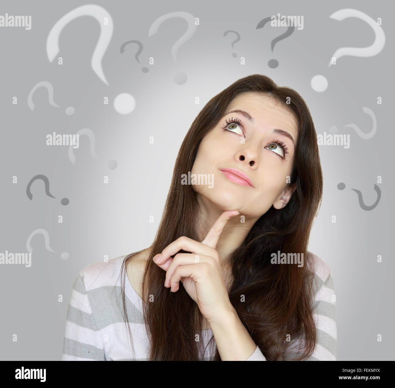 Beautiful girl with questions thinks above her head looking up isolated on grey background Stock Photo