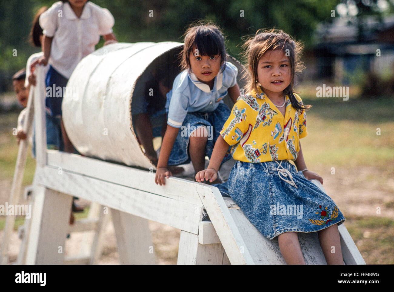 Local village school children play on a wooden slide with a play tunnel  made from a metal barrel in a school playground in Laos Stock Photo - Alamy