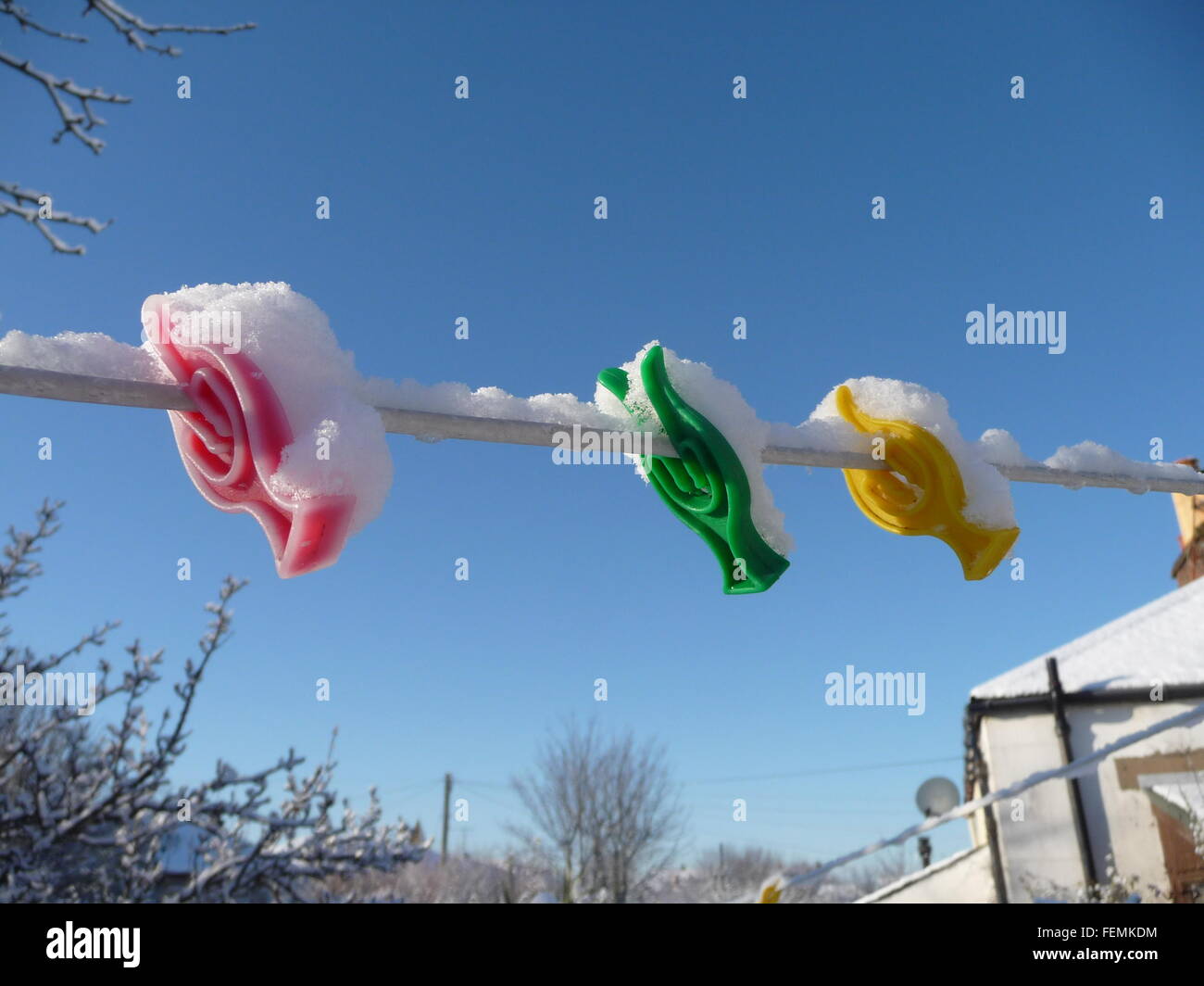 Shot of brightly colored plastic clothes pegs and line caked in snow, against a bright blue sky Stock Photo