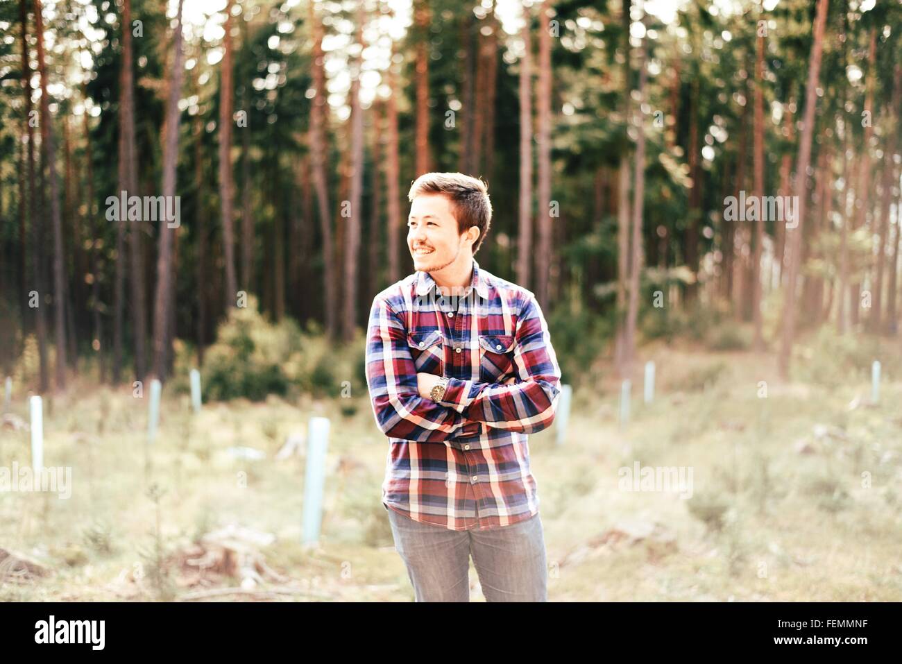 Happy Man Standing With Arms Crossed In Forest Stock Photo