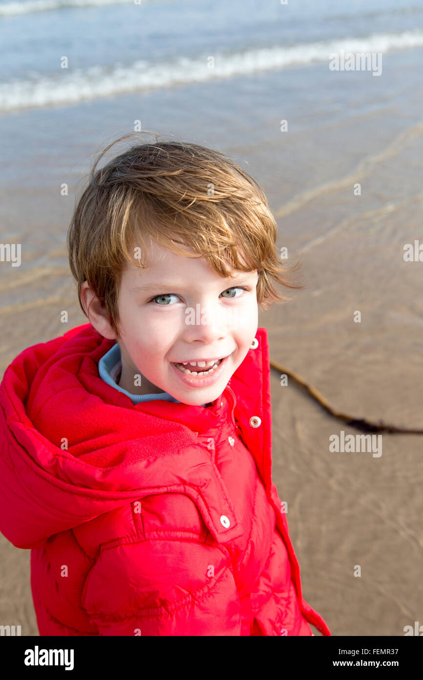 Little boy in a red coat on the beach, smiling at the camera Stock