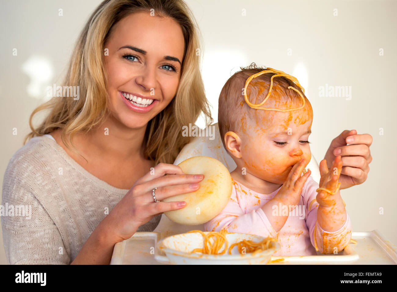 Mother laughing as she tries to clean her messy baby daughter, who has