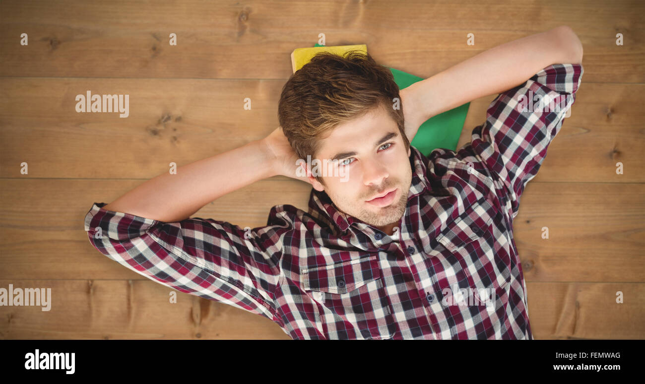 Composite image of hipster with hands behind head lying on hardwood floor Stock Photo