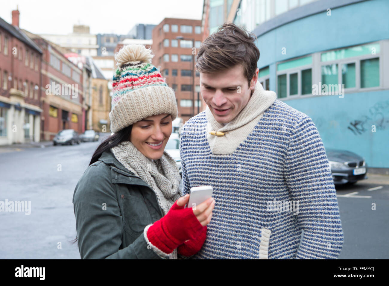 Young couple standing together in the cold weather, looking at a smartphone Stock Photo
