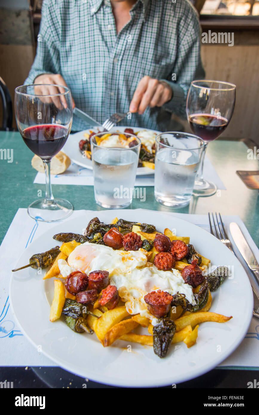 Fried eggs with chips, chorizo and Padron peppers in a restaurant. Stock Photo