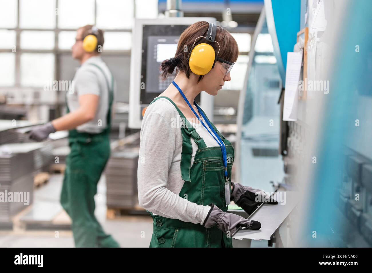 Female worker with ear protectors holding metal part in factory Stock Photo