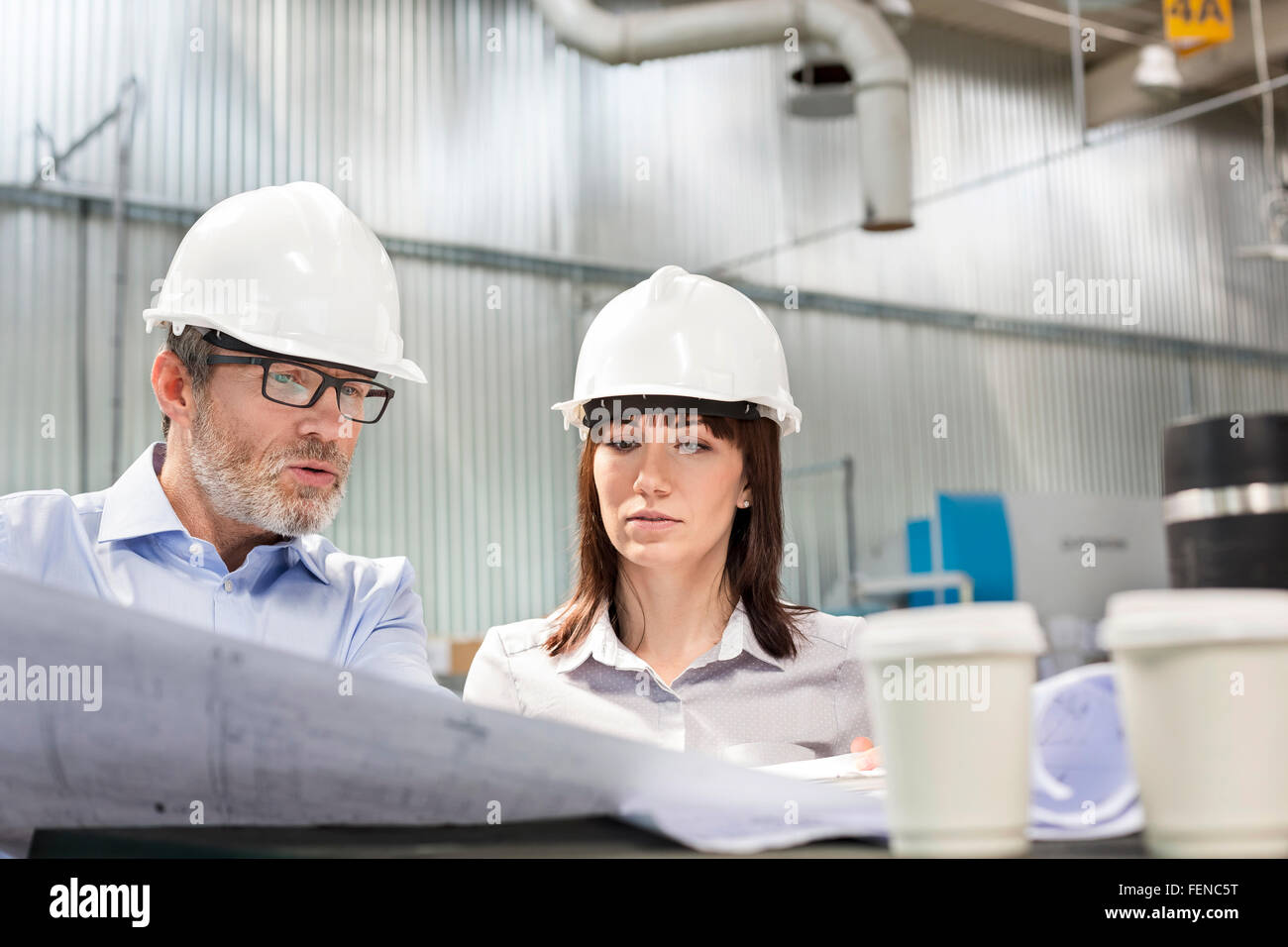 Engineers in hard-hats viewing blueprints in factory Stock Photo