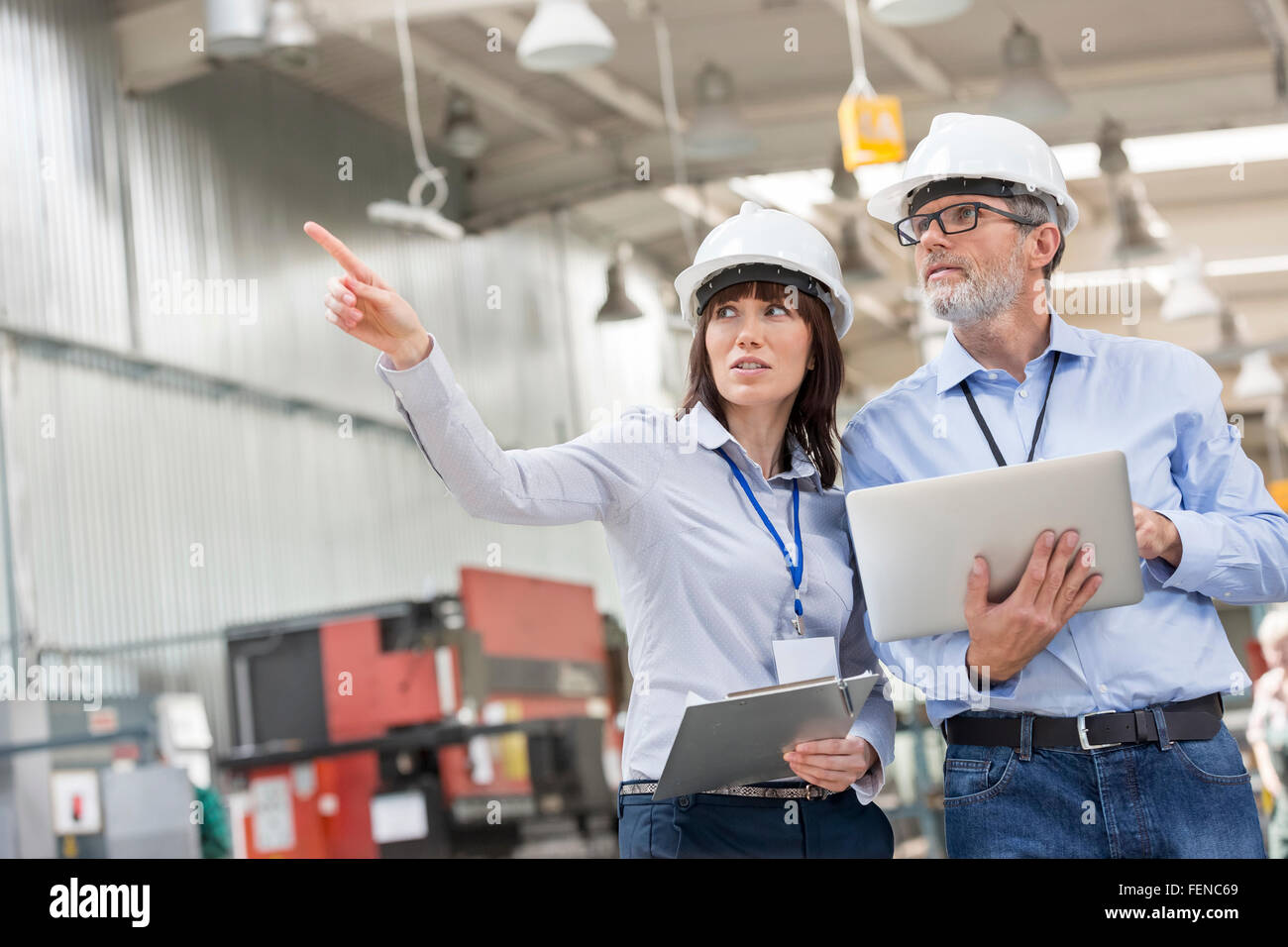 Engineers with laptop and clipboard pointing in factory Stock Photo