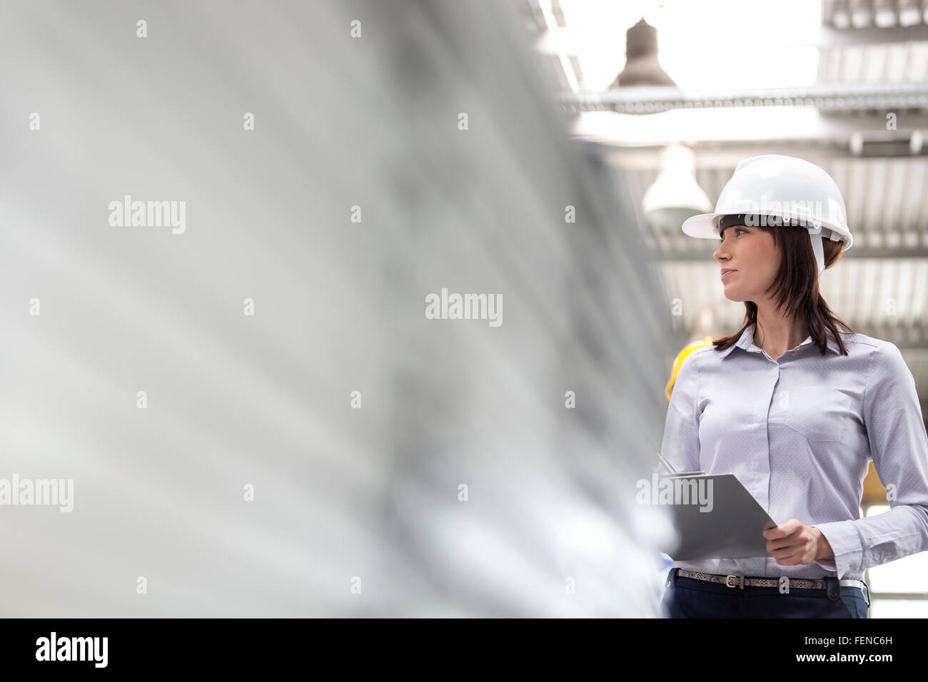 Businesswoman in hard-hat and clipboard working in factory Stock Photo