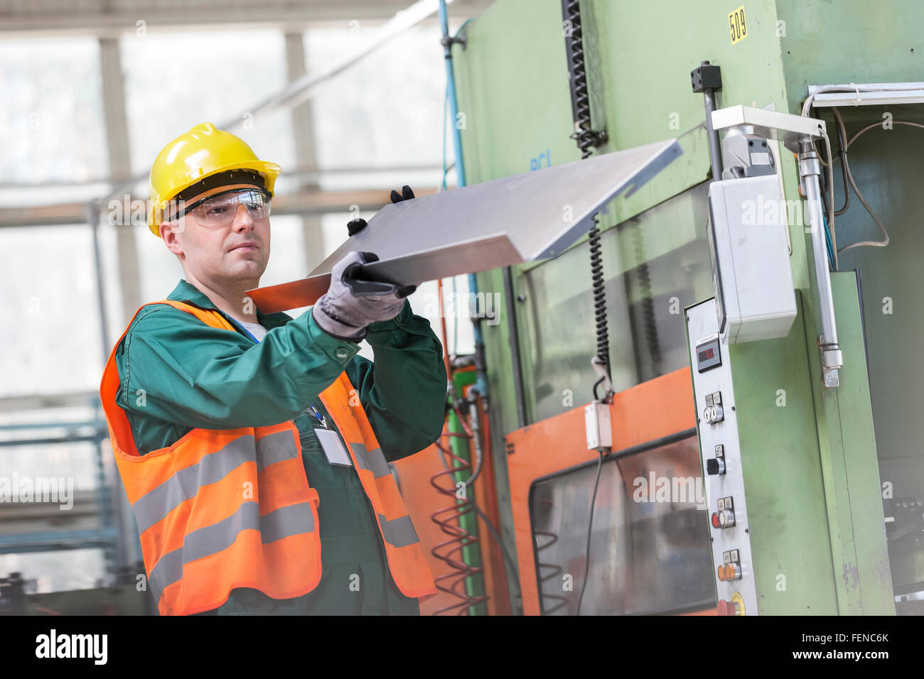 Worker in protective workwear examining steel part in factory Stock Photo