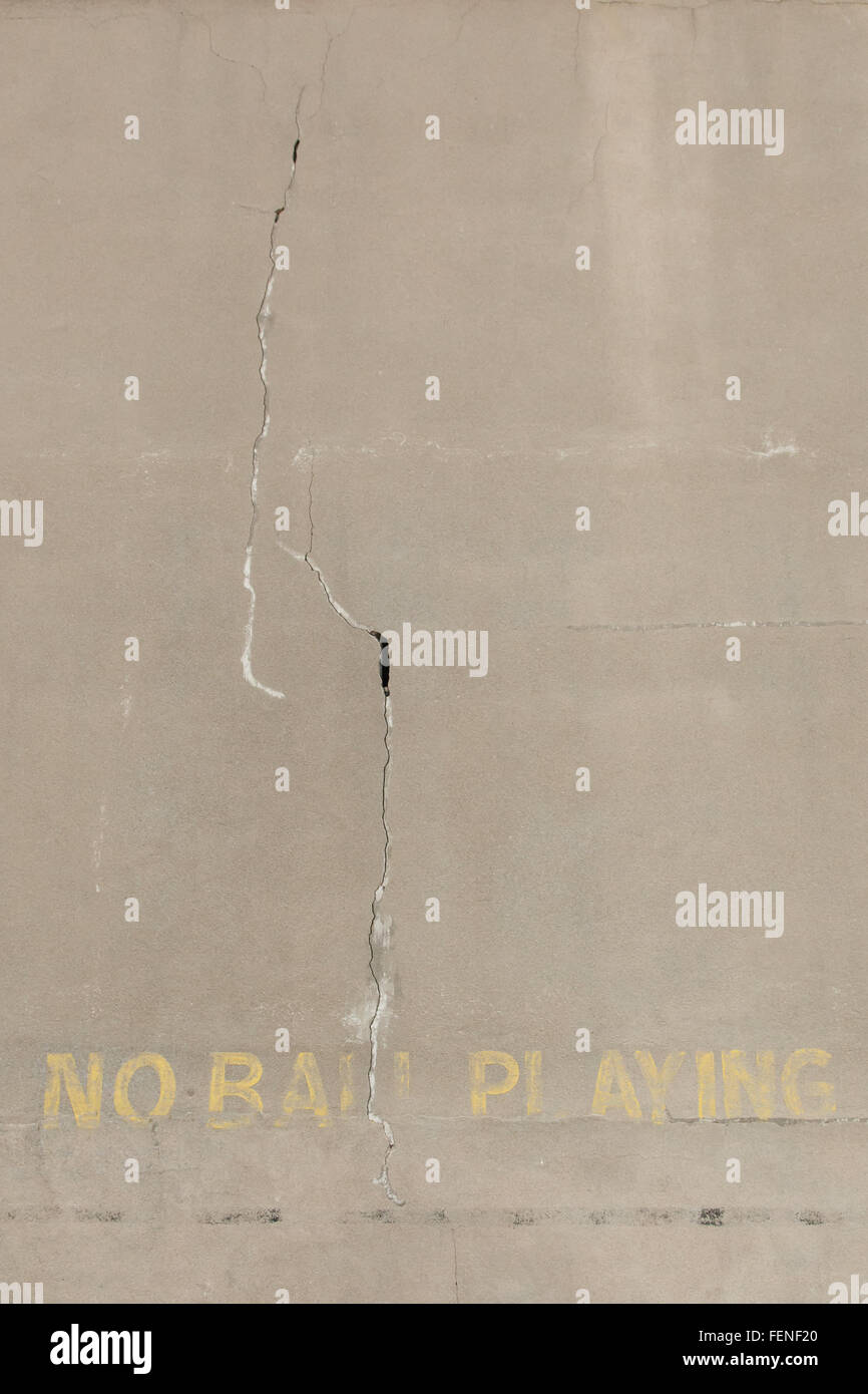 A cracked, old concrete wall says 'No Ball Playing.' Stock Photo