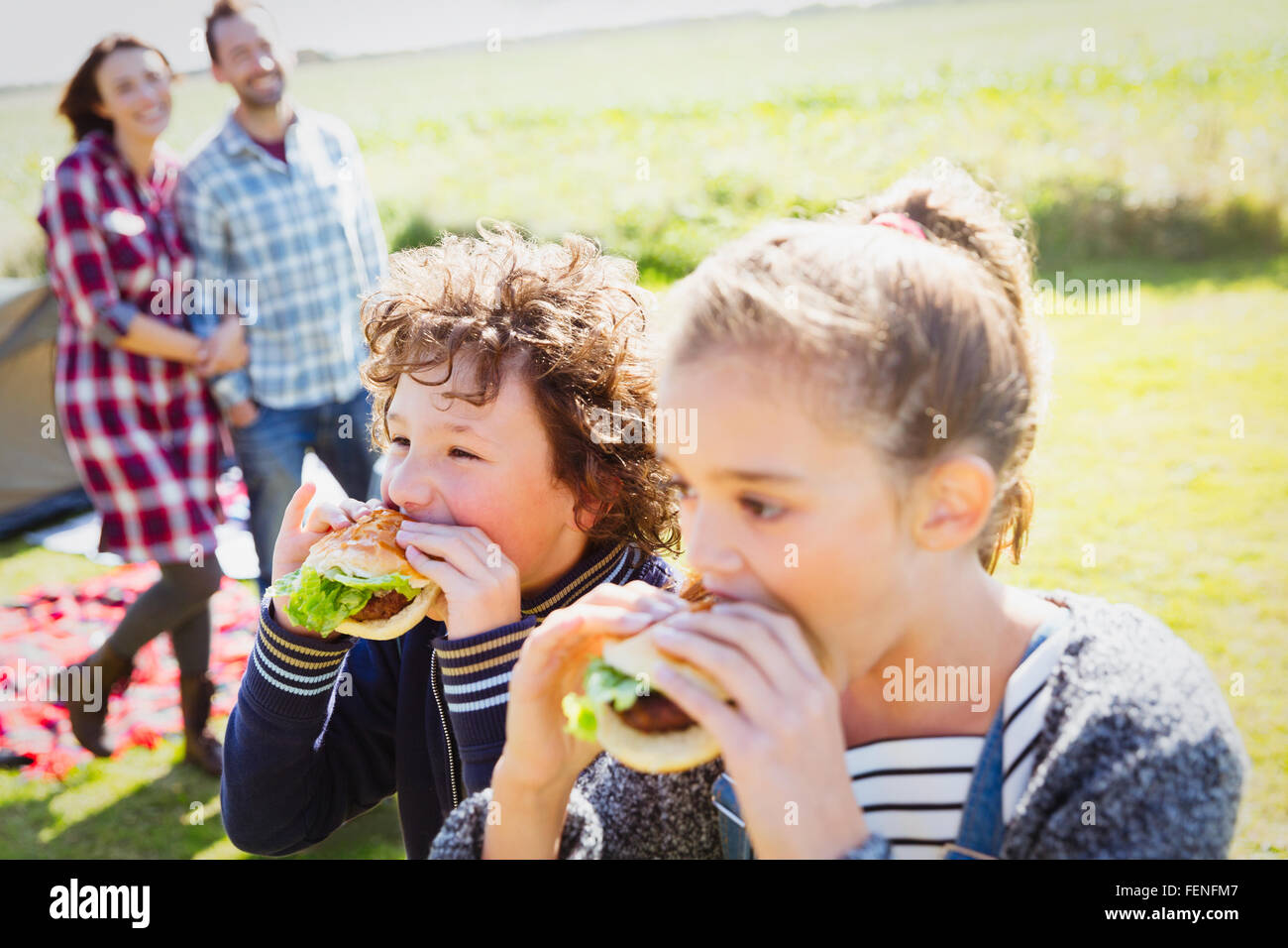 Brother and sister eating hamburgers at sunny campsite Stock Photo