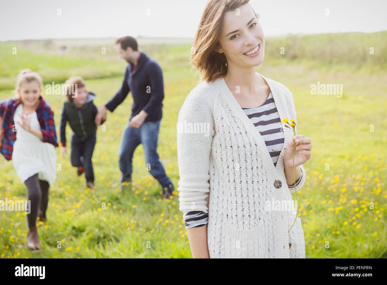 Portrait smiling woman holding wildflower in meadow with family Stock Photo