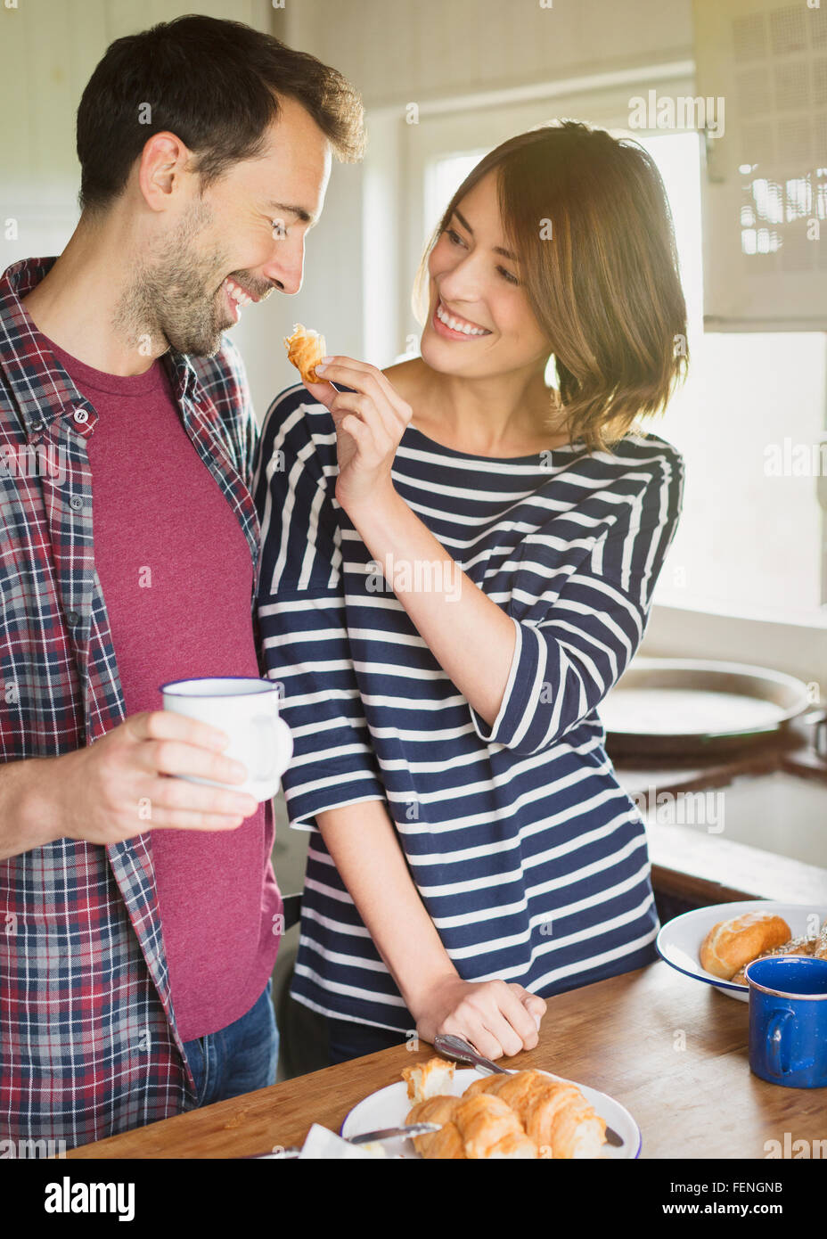 Girlfriend feeding boyfriend croissant in kitchen Stock Photo